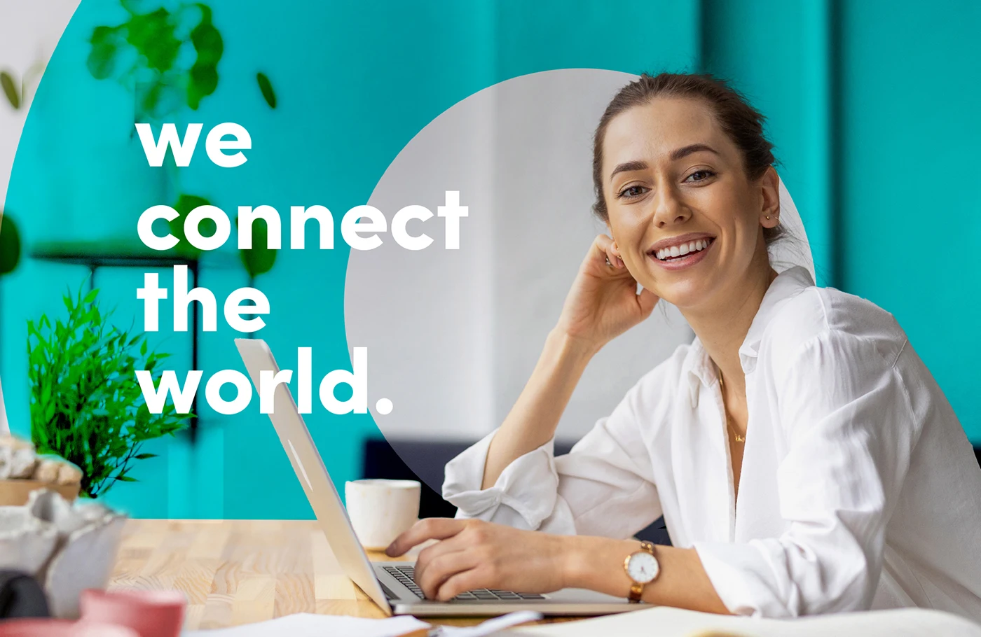 Eine junge Frau sitzt am Schreibtisch vor dem Laptop und lächelt in die Kamera.